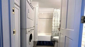 A compact bathroom with a washing machine, a bathtub, and a toilet. - Studio Steps To The Sand - Spacious, Clean, Cozy (Manhattan Beach)