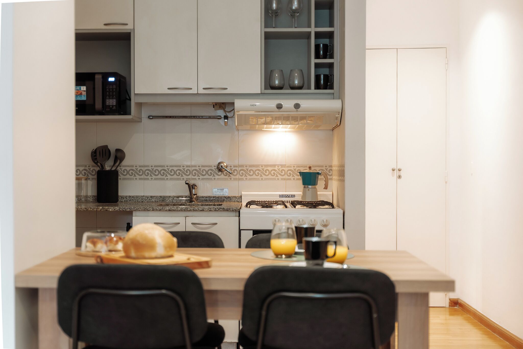 Een compacte keuken met een magnetron, fornuis en een klein eetgedeelte met stoelen en een tafel.