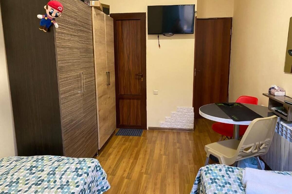 A room with two beds, a TV mounted on the wall, a wooden wardrobe, and a small table with chairs.