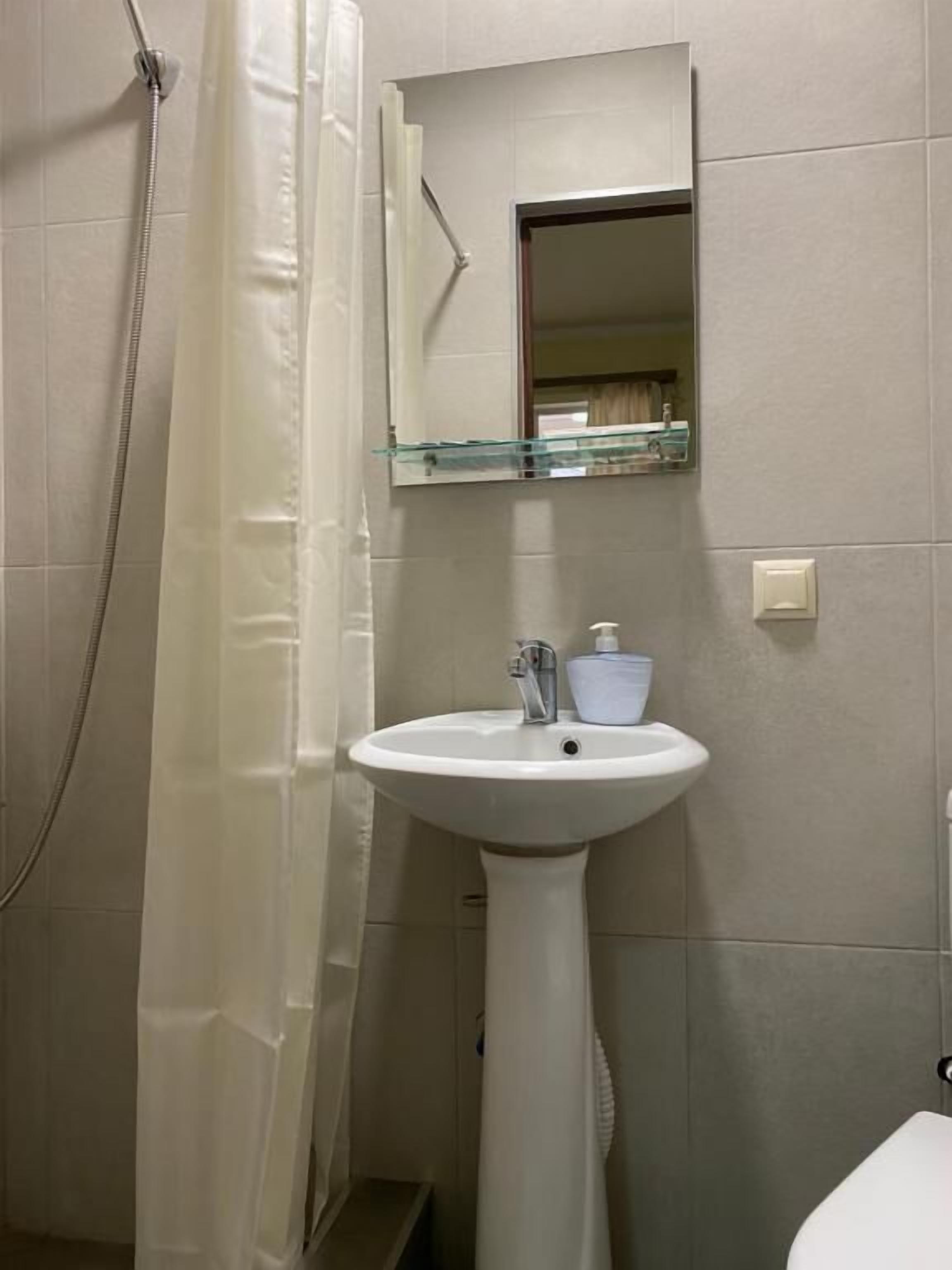 A bathroom with a pedestal sink, a glass shelf above the mirror, and a shower curtain.