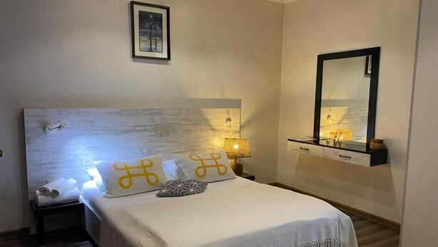 A neatly arranged bedroom with a large bed, a bedside table, a nightstand, a wall-mounted shelf, and a mirror. - Guest House Aygestan Hotel (Yerevan)