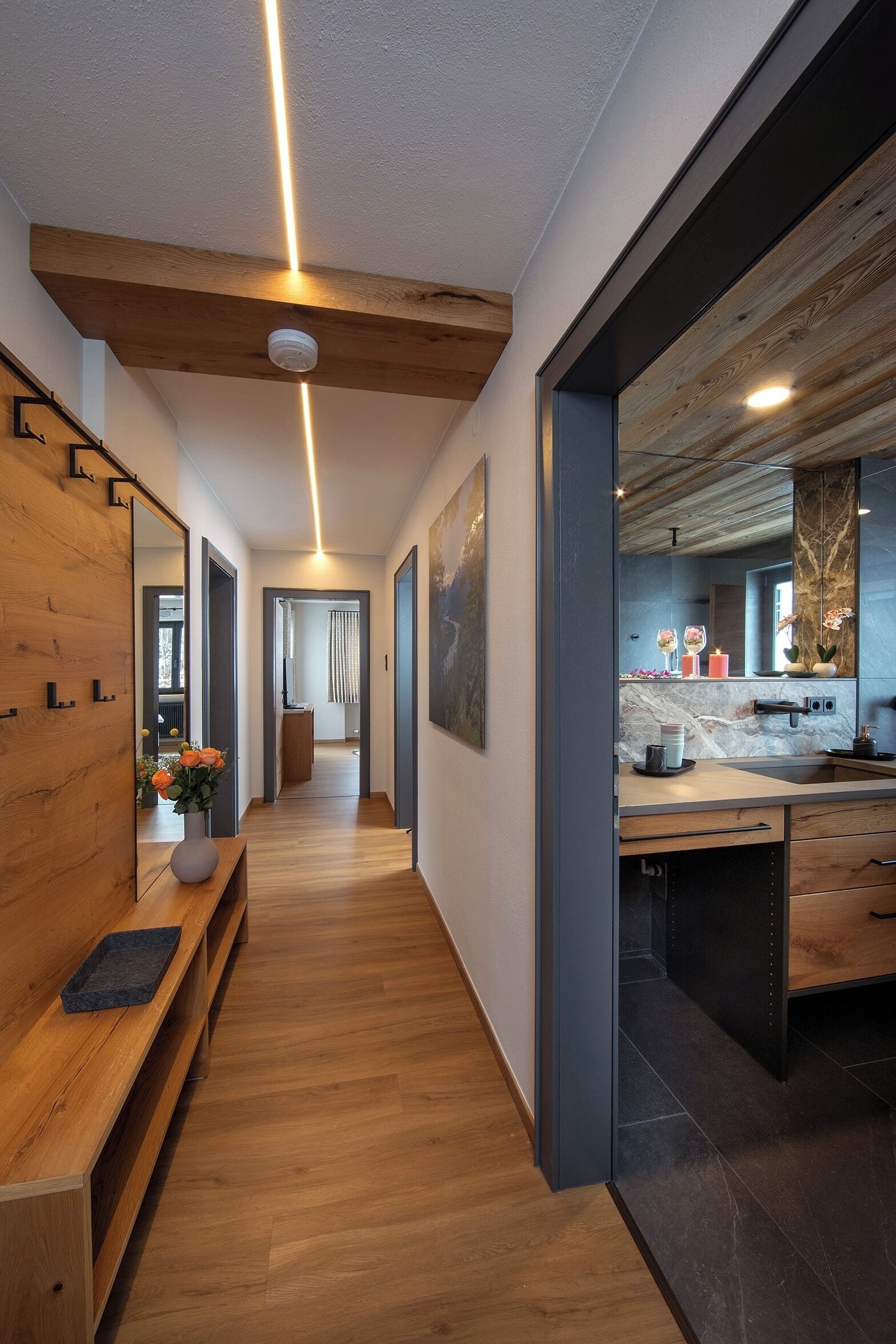 Um interior moderno com um banco de madeira, cozinha com bancada de mármore e corredor que dá para outro quarto.