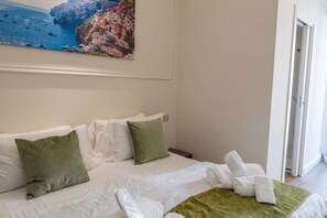 A hotel room with a bed, pillows, a towel, and a painting of a coastal scene. - A CASA TUA  (Naples)