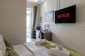 Una camera d'albergo con un letto, una scrivania, una televisione e una finestra con tende.
