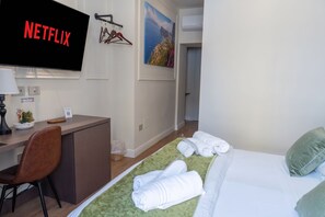 A hotel room with a bed, a desk with a chair, a television displaying 'NETFLIX', a painting on the wall, and a green rug. - A CASA TUA  (Naples)