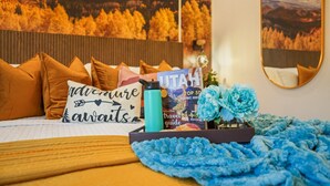 Een keurig opgemaakt bed met een reisgids, een waterfles en een decoratief kussen.