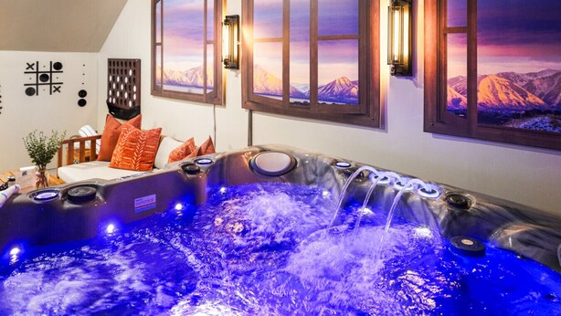 Een hottub met uitzicht op de bergen, een houten bankje en een muur met ingelijste foto's.
