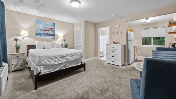 A bedroom with a bed, bedside tables, a dresser, a chair, a window, and a painting on the wall. - Oak Shores Studio 4 | Just a Short Walk to the Beach! (Biloxi)