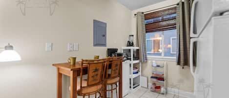 Una cocina compacta con comedor, refrigerador, cafetera y ventana con cortinas.