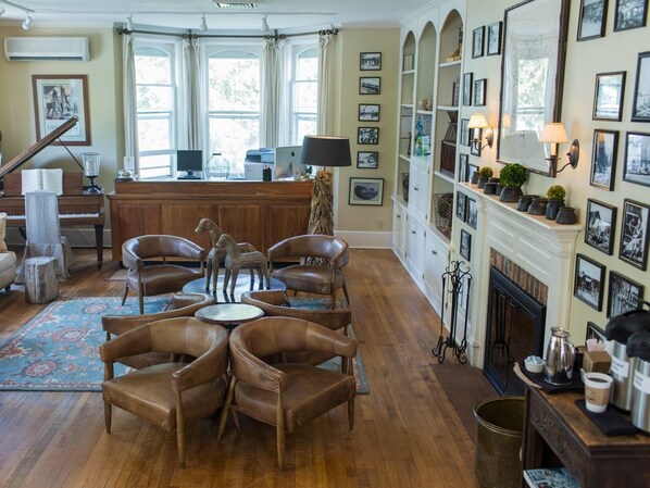 A spacious living room with a piano, leather chairs, a fireplace, and a wall adorned with framed pictures.