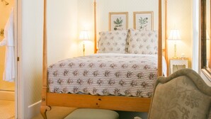 Una cama con dosel, ropa de cama floral, dos lámparas de noche e impresiones botánicas enmarcadas en la pared.
