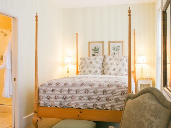 Una cama con dosel, ropa de cama floral, dos lámparas de noche e impresiones botánicas enmarcadas en la pared.