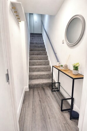 A staircase leading to a landing with a wooden floor, a small table with a mirror, and a potted plant. - 2BR apartment near Stratford East London (London)