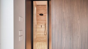 Une douche à l’italienne étroite, avec un encadrement en bois, un mur texturé et une seule pomme de douche.