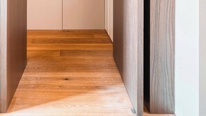 Un couloir étroit, doté d’un plancher en bois et terminé par une porte sobre.