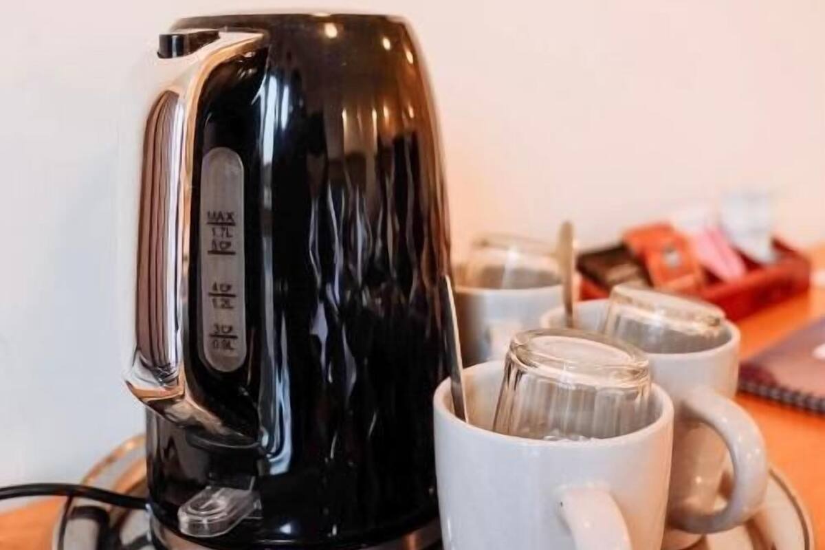 Una tetera eléctrica negra sobre una bandeja con dos tazas blancas.