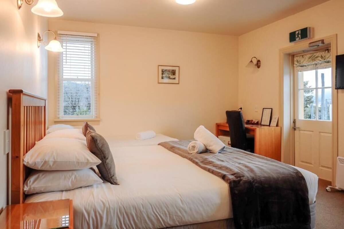Un dormitorio con cama, mesita de noche, lámpara y ventana.