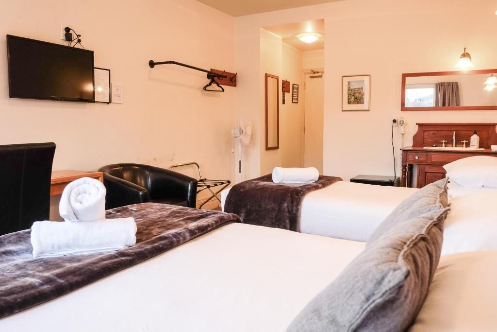 Habitación de hotel con dos camas, un televisor montado en la pared, un escritorio con silla y un baño con espejo y lavamanos.