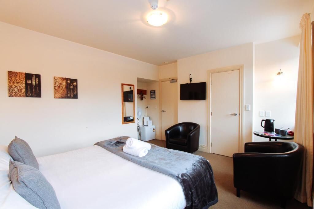 Habitación de hotel con cama, escritorio, silla, televisor y obras de arte en la pared.