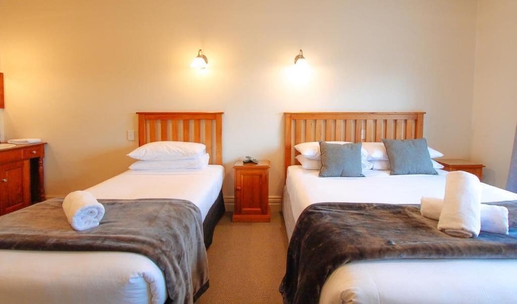 A hotel room with two single beds, each with a wooden headboard, a nightstand, and a wall-mounted lamp.