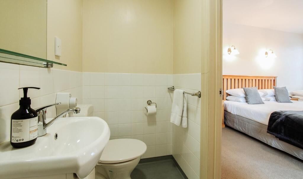 Een badkamer met een wastafel en toilet, en een bed in de aangrenzende kamer.