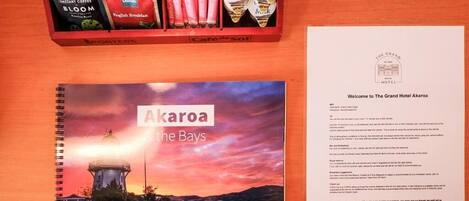 En brochure for The Grand Hotel Akaroa The Bays, en ringperm med et naturskønt solnedgangsbillede, samt en bakke med instantkaffe og mælkeposer.