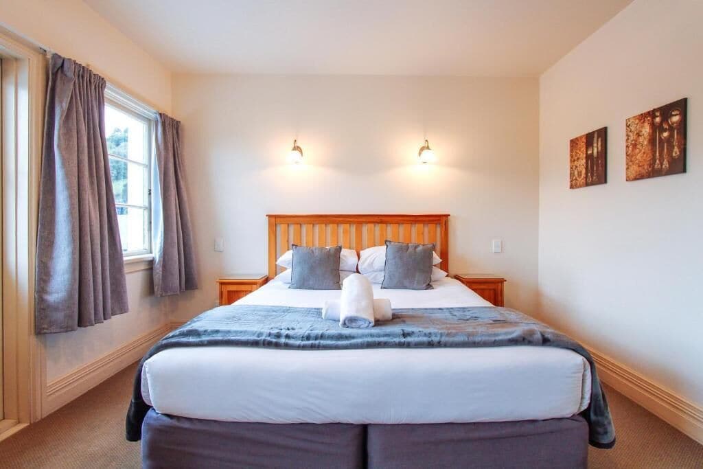 A hotel room with a large bed, two bedside tables, a window with curtains, and wall-mounted lights.