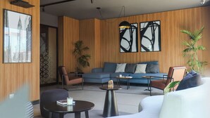 Een moderne woonkamer met een bank, fauteuils, een salontafel en een groot raam met abstracte kunst.