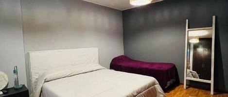 Een slaapkamer met een bed, nachtkastje, kapstok en spiegel.