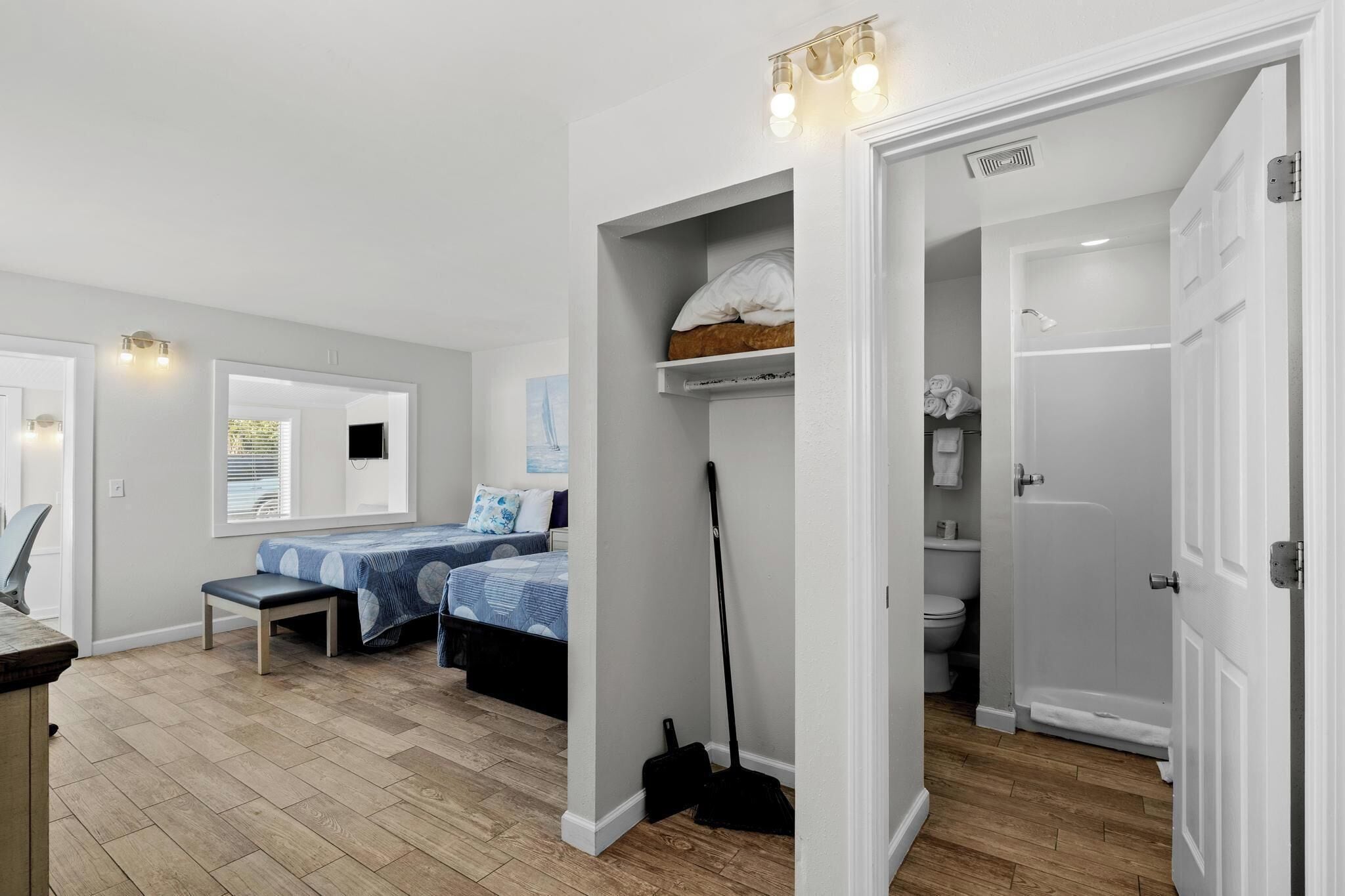 A bedroom with a bed, a bench, a closet, and a bathroom with a shower and toilet.