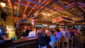 Un espace bar avec des poutres en bois au plafond, des luminaires suspendus et des clients assis à des tables.