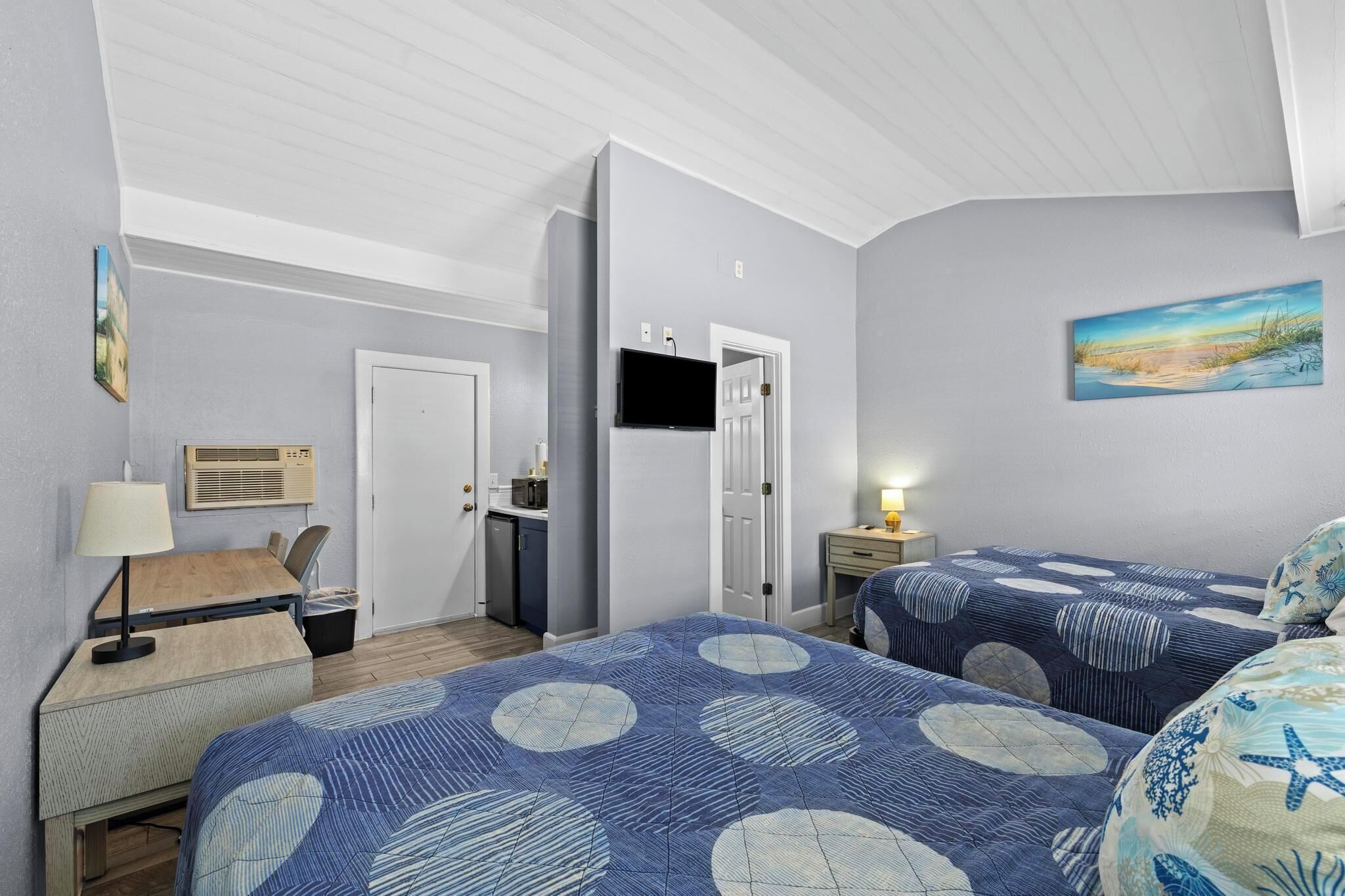 A bedroom with two beds, a desk, a chair, a TV, and a painting on the wall.