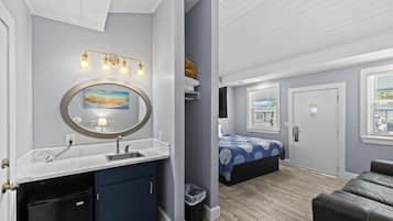 A room with a sink, mirror, and a bed with a blue and white patterned bedspread.