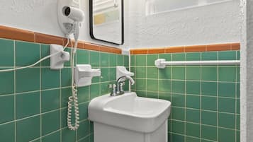 Une salle de bain avec un lavabo blanc, des murs recouverts de carreaux verts, un sèche-cheveux et un miroir.