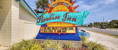 A sign for Paradise Inn with a sun motif, listing room numbers and names.