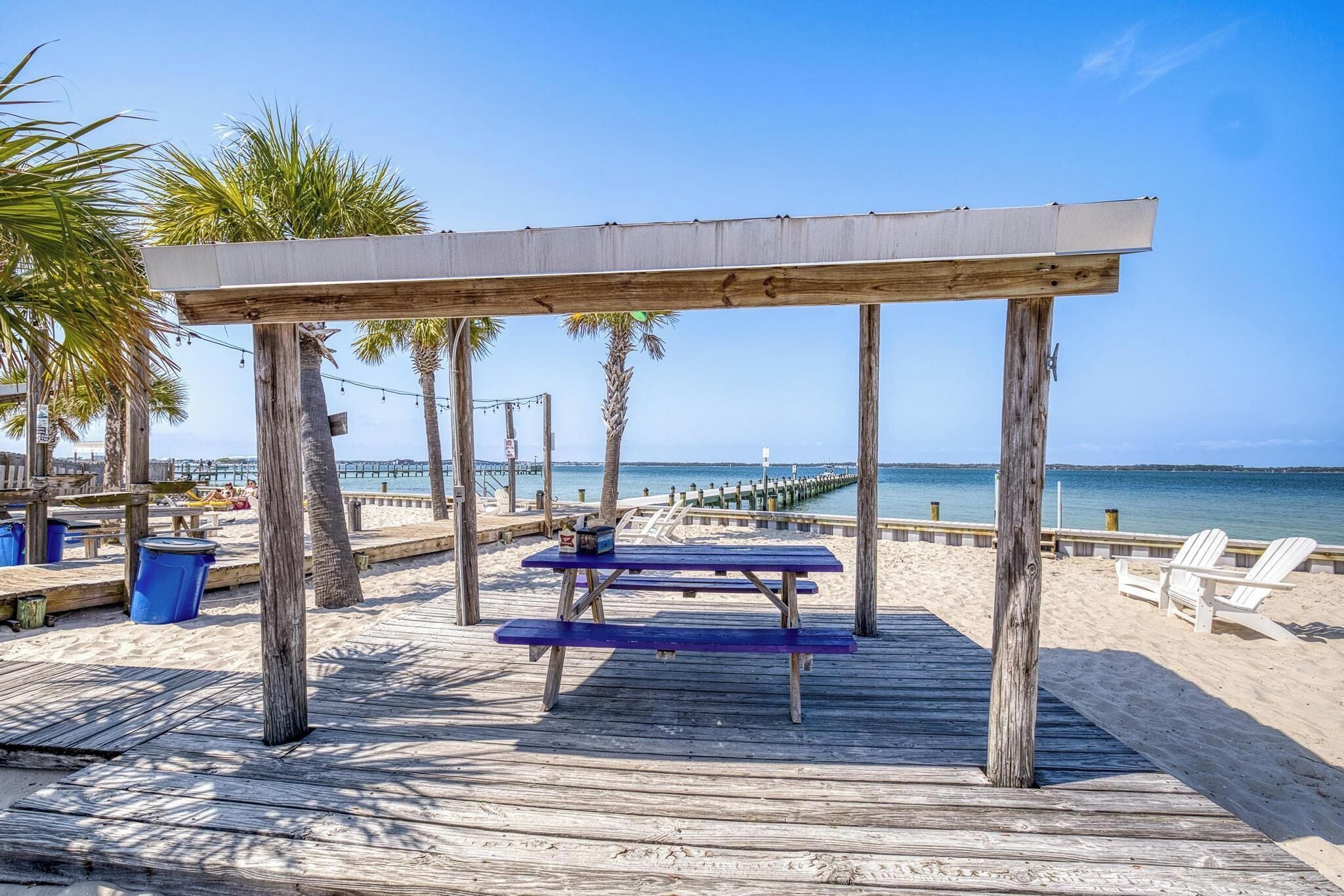 A wooden deck with picnic tables, beach chairs, and palm trees.