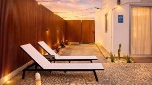 Un espace aménagé au bord de la piscine, avec des chaises longues, une piscine et des guirlandes lumineuses.