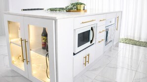 Une cuisine moderne avec des meubles blancs, des poignées dorées et un four à micro-ondes encastré.