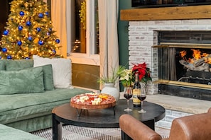 Ein gemütliches Wohnzimmer mit Weihnachtsbaum, Kamin und rundem Tisch mit Wurstplatte und Weingläsern.