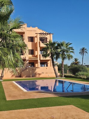 A building with a pool, surrounded by palm trees and greenery. - Golf & Comfort: Luxury apartment in Los Alcázares (Los Alcázares)