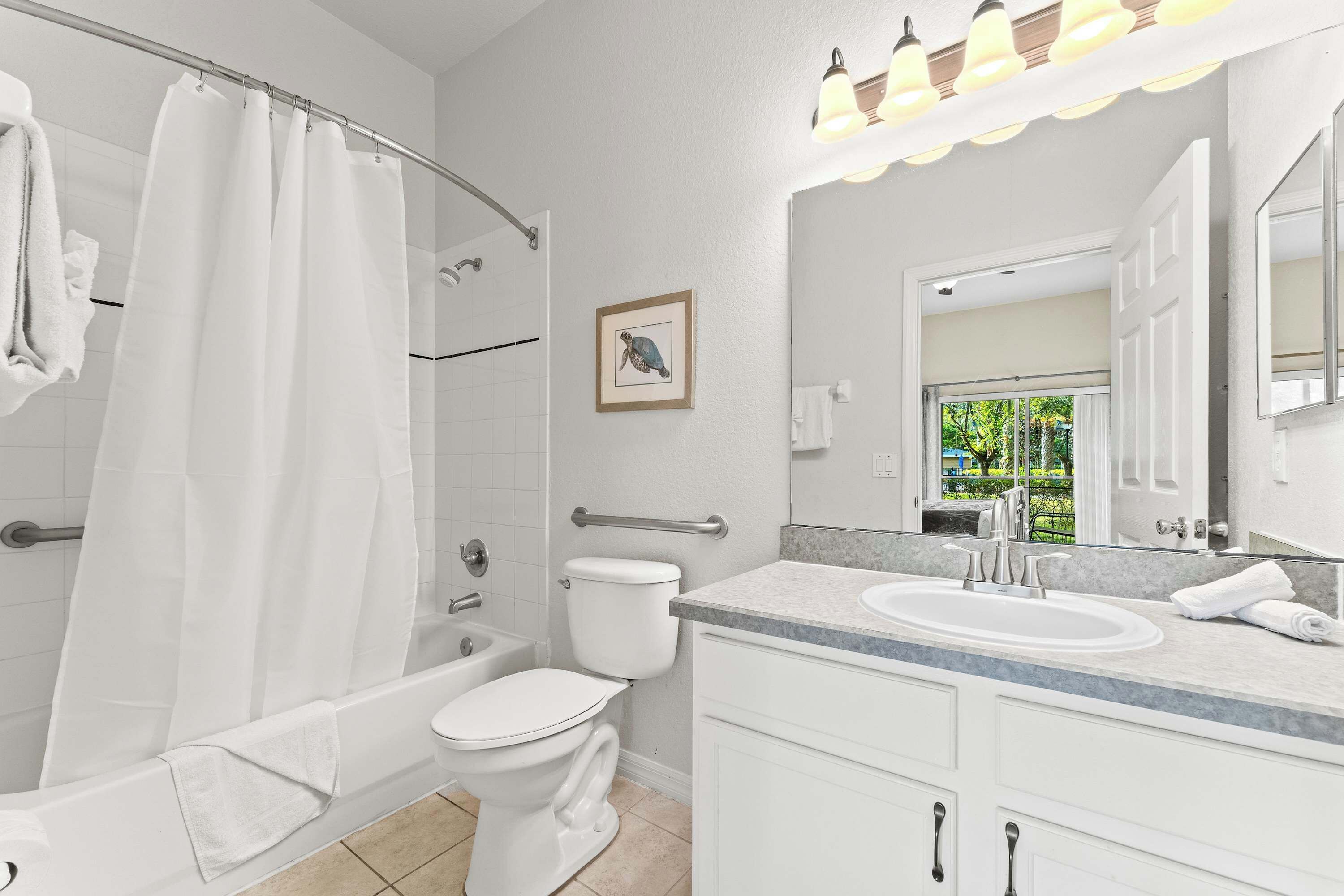 Et moderne badeværelse med badekar, toilet og håndvask, komplet med bruseforhæng, et indrammet billede og en vaskebord med spejl.