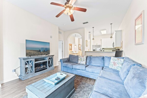 A living room with a sectional sofa, a coffee table, a TV, and a ceiling fan. - Serenity at Bahama Bay For 8 (Davenport)