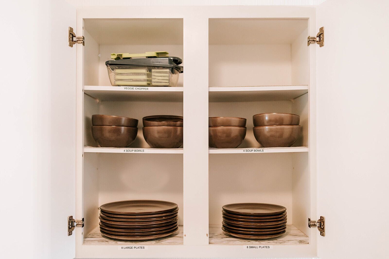 A kitchen cabinet with four soup bowls, eight large plates, and eight small plates.