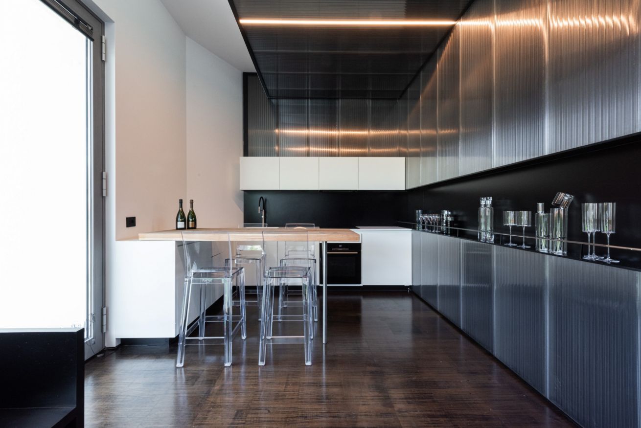 A modern kitchen with a central island, bar stools, and wine glasses on the wall.