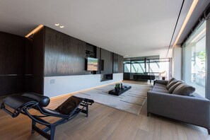 A modern living room with a sofa, a recliner, a flat-screen TV, and a large window.