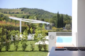 A patio area with a grill, a white umbrella, and a view of a pool and hills. - Villa Bilor Luxe by MMega (Subbiano)