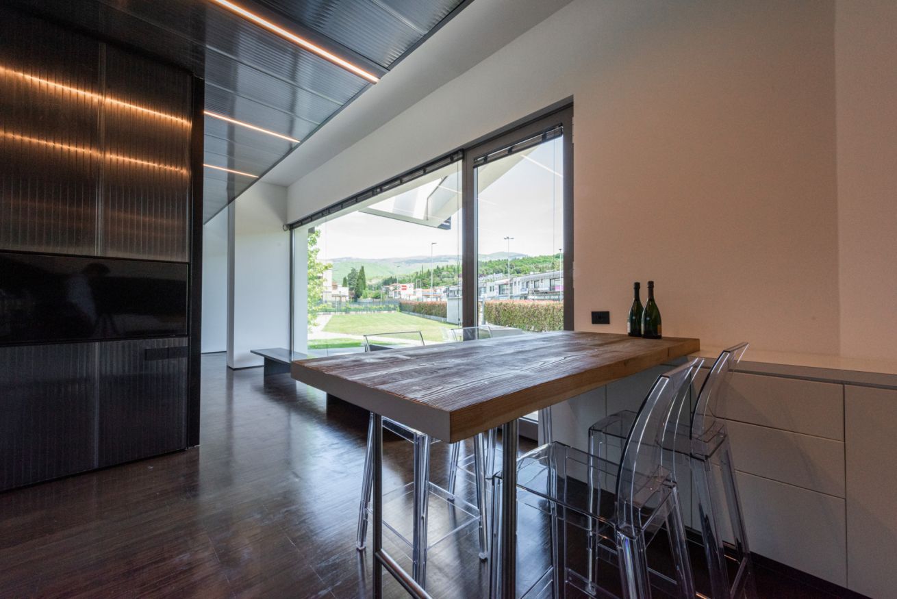 Een moderne keuken met een houten tafel en transparante stoelen, grote ramen met uitzicht op de omgeving.