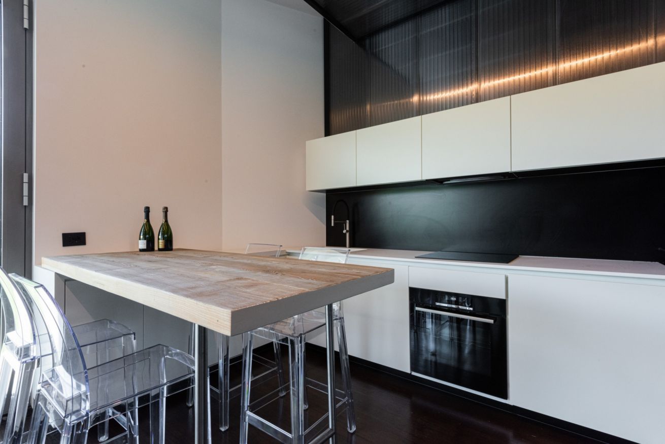 A modern kitchen with a wooden table, clear chairs, and a built-in oven.
