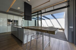 A modern kitchen with a wooden table, clear chairs, and a large window.