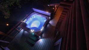 Ein Whirlpool auf einer Holzterrasse bei Nacht, umgeben von Bäumen.